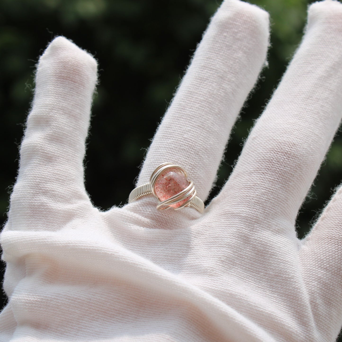 Beautiful strawberry quartz ring wrapped in silver on a model's finger outdoors