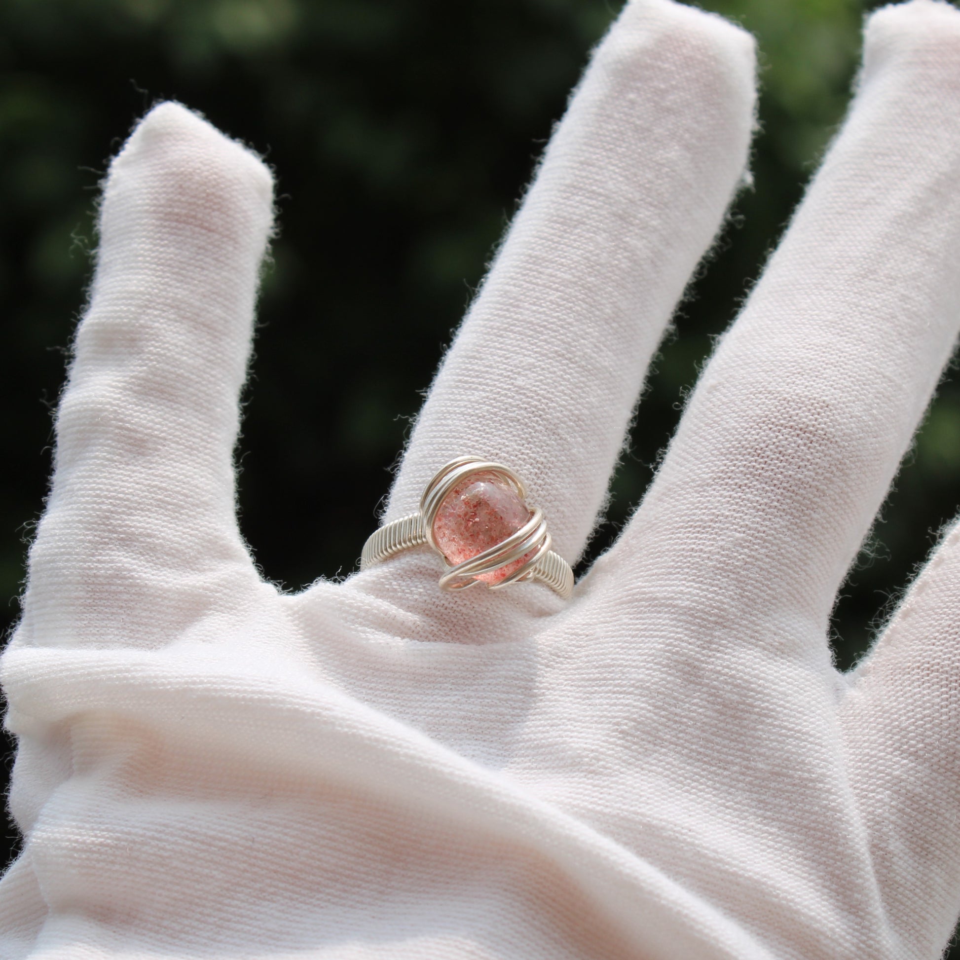 Beautiful strawberry quartz ring wrapped in silver on a model's finger outdoors