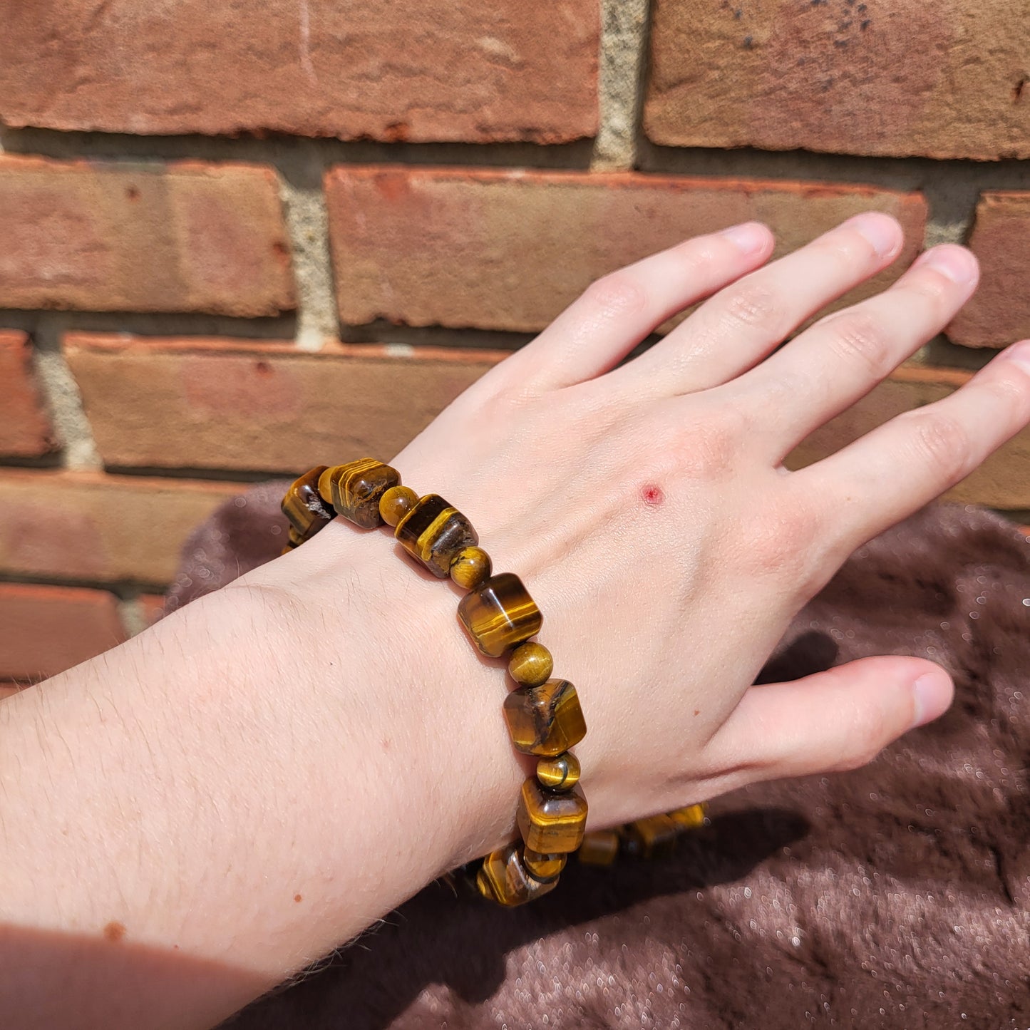 Tiger eye cube bracelet worn on a hand against a brick wall background