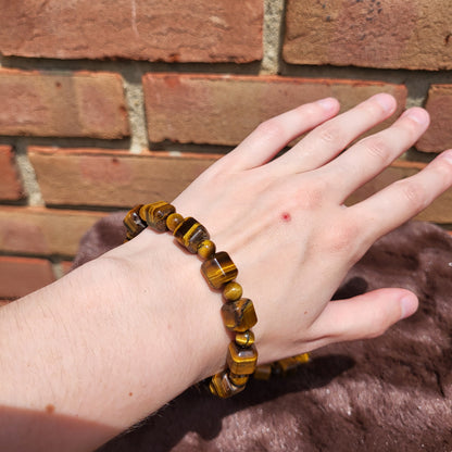 Tiger eye cube bracelet worn on a hand against a brick wall background