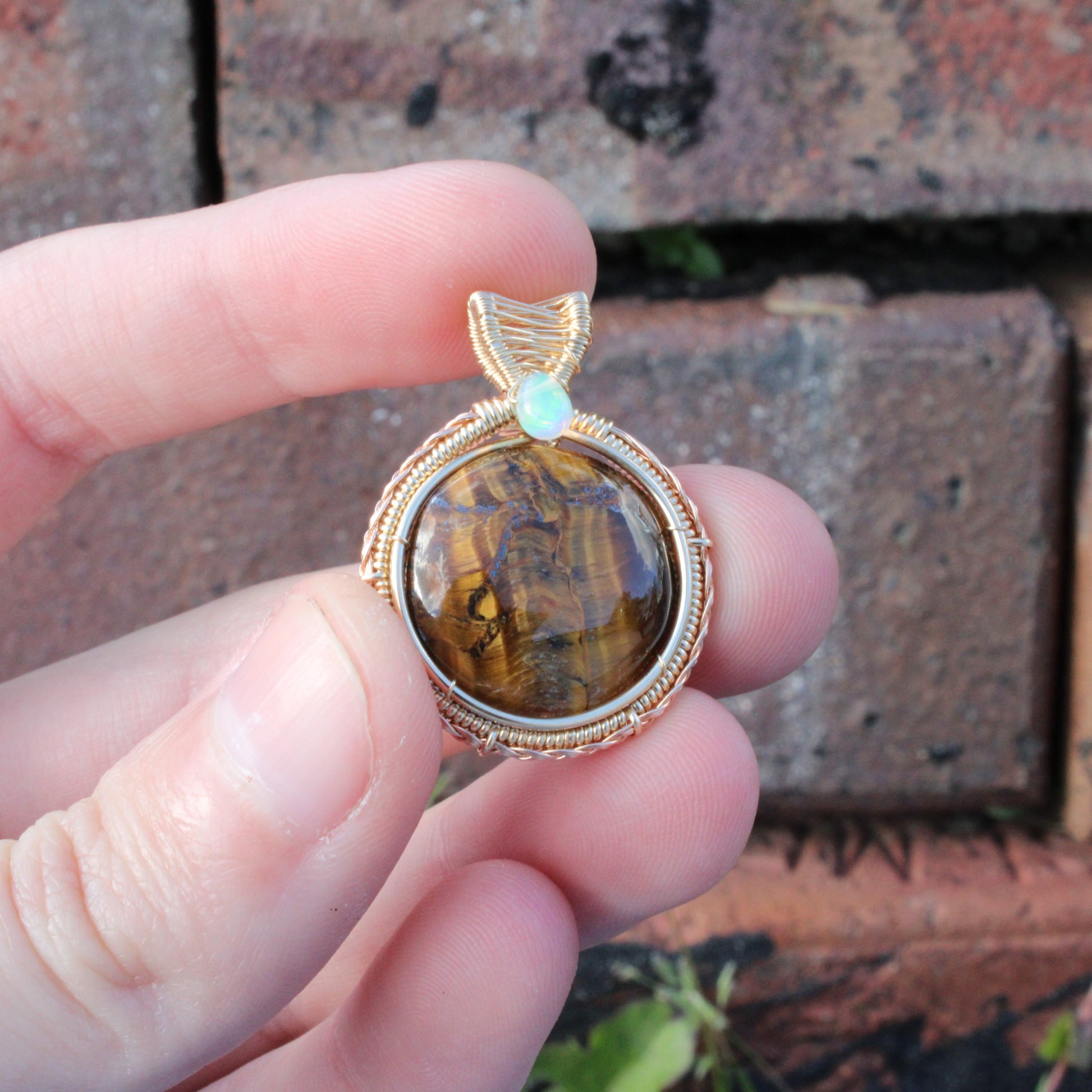 Tiger eye Ethiopian Opal 14k yellow and rose gold fill pendant held by hand against a brick background