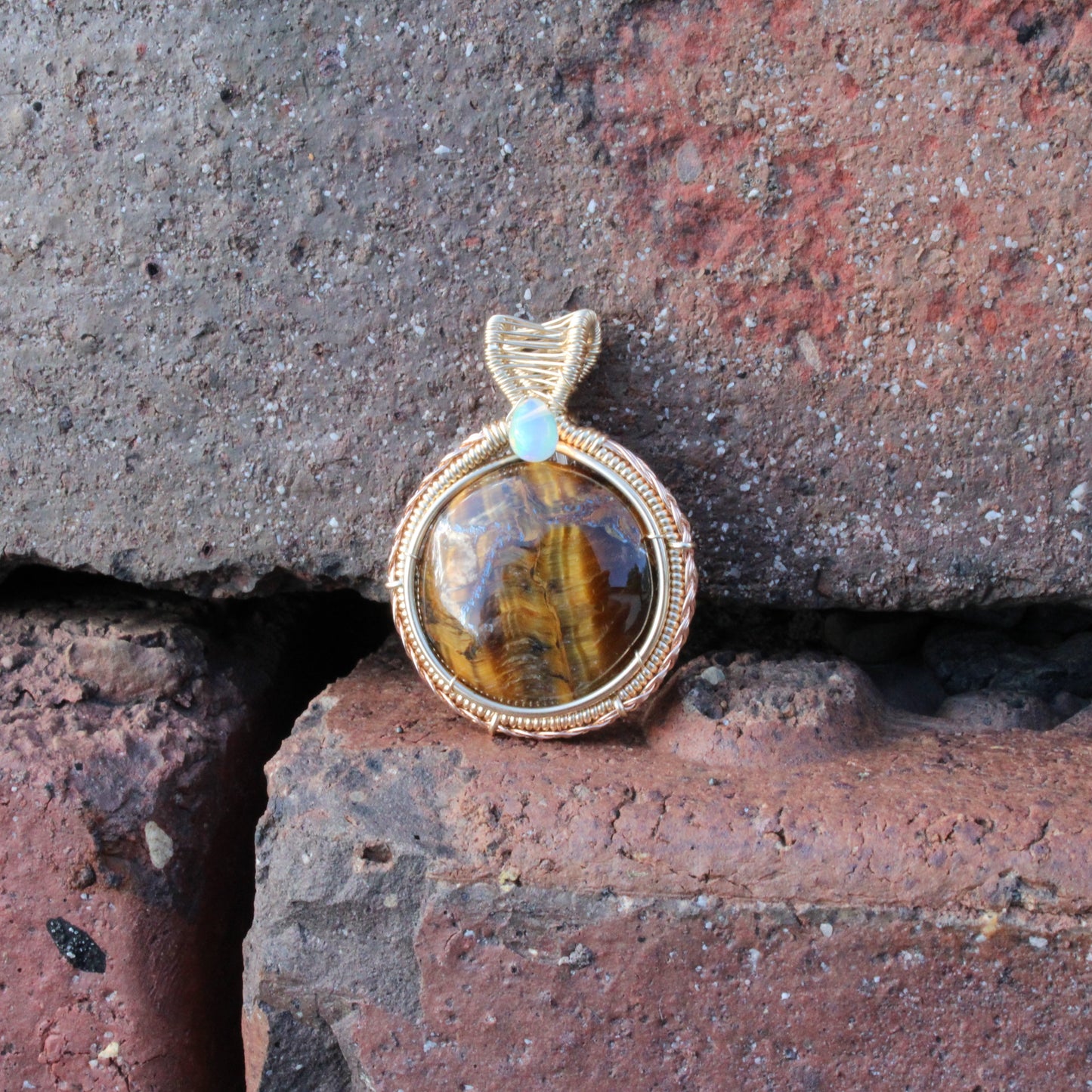 Tiger eye Etheopian Opal 14k yellow and rose gold fill pendant showcased on textured brick background
