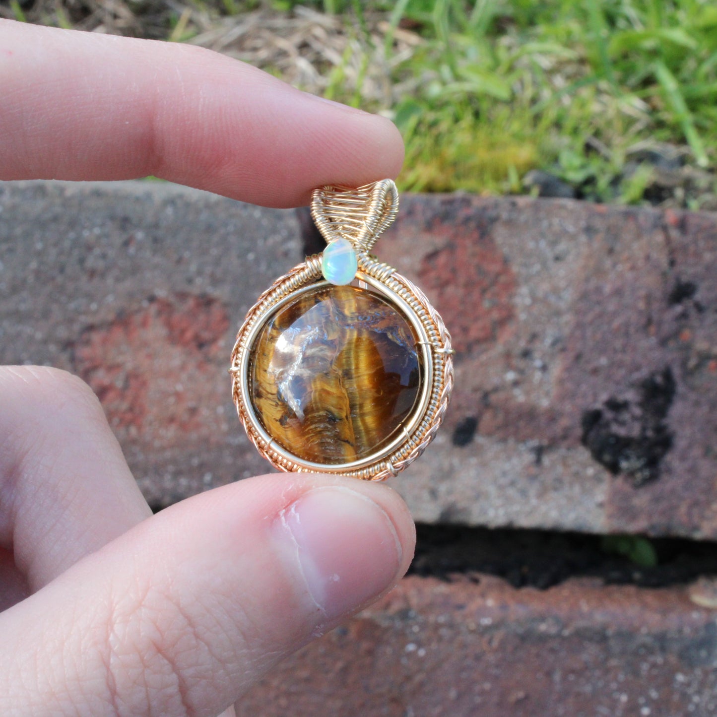 Tiger eye Ethiopian Opal 14k yellow and rose gold fill pendant held in hand with a natural background