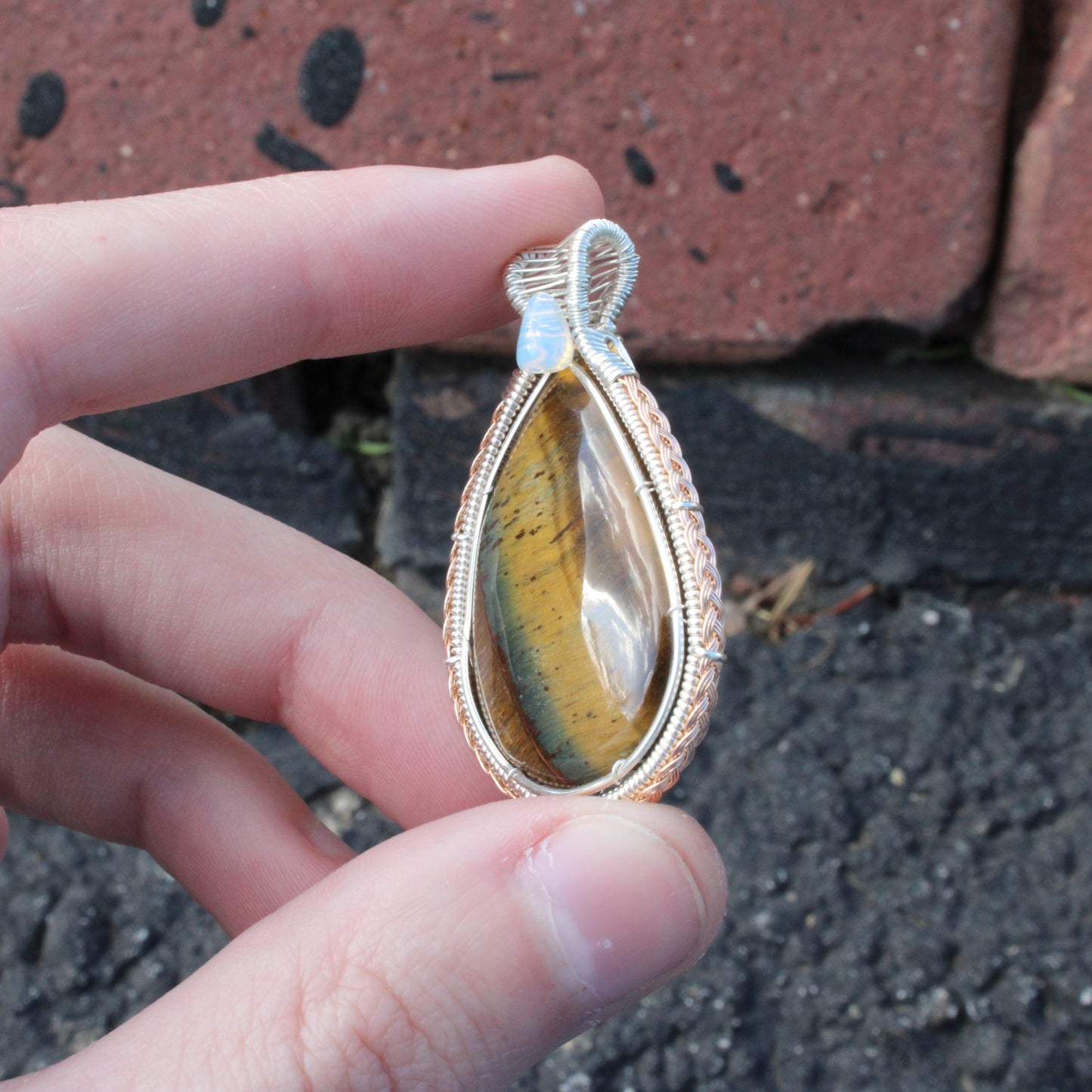 Tiger eye, Ethiopian opal sterling silver pendant held between fingers, showcasing unique design.