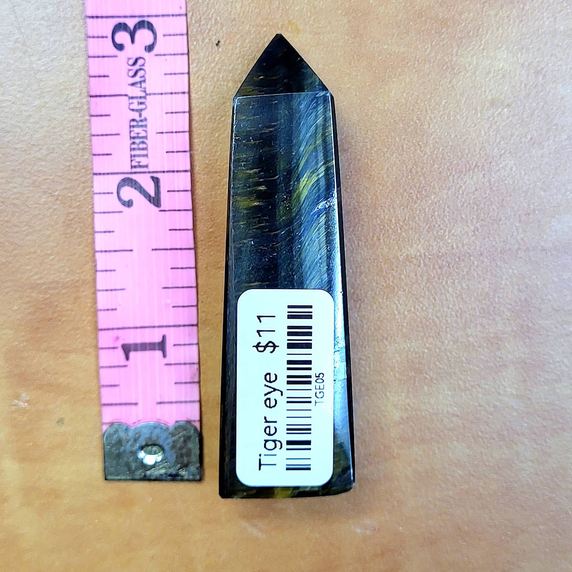 Tiger's eye tower crystal displayed next to a ruler for size reference in a natural setting