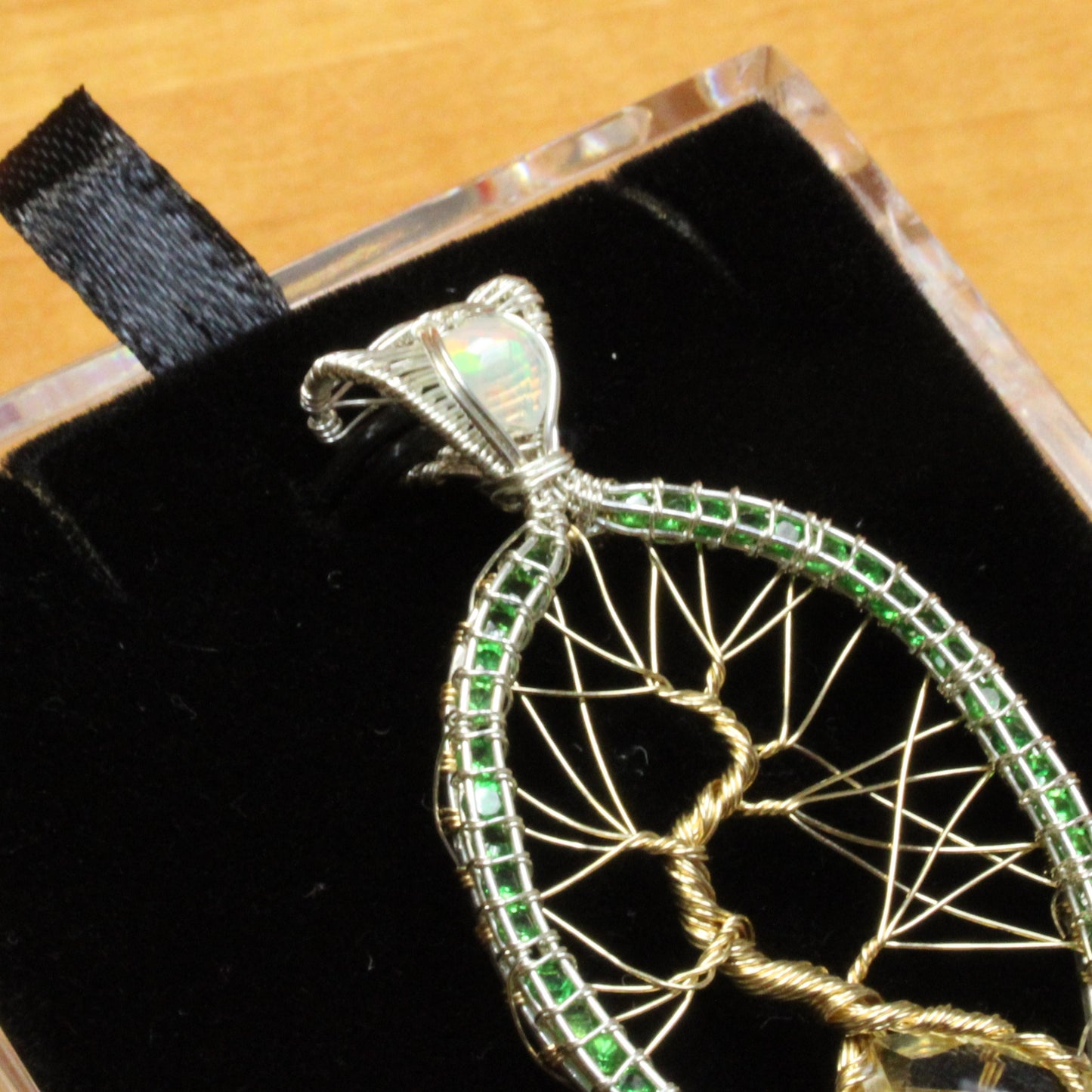 Tsavorite tree of life pendant intricately crafted with green stones and silver wire, elegantly displayed on a black velvet background