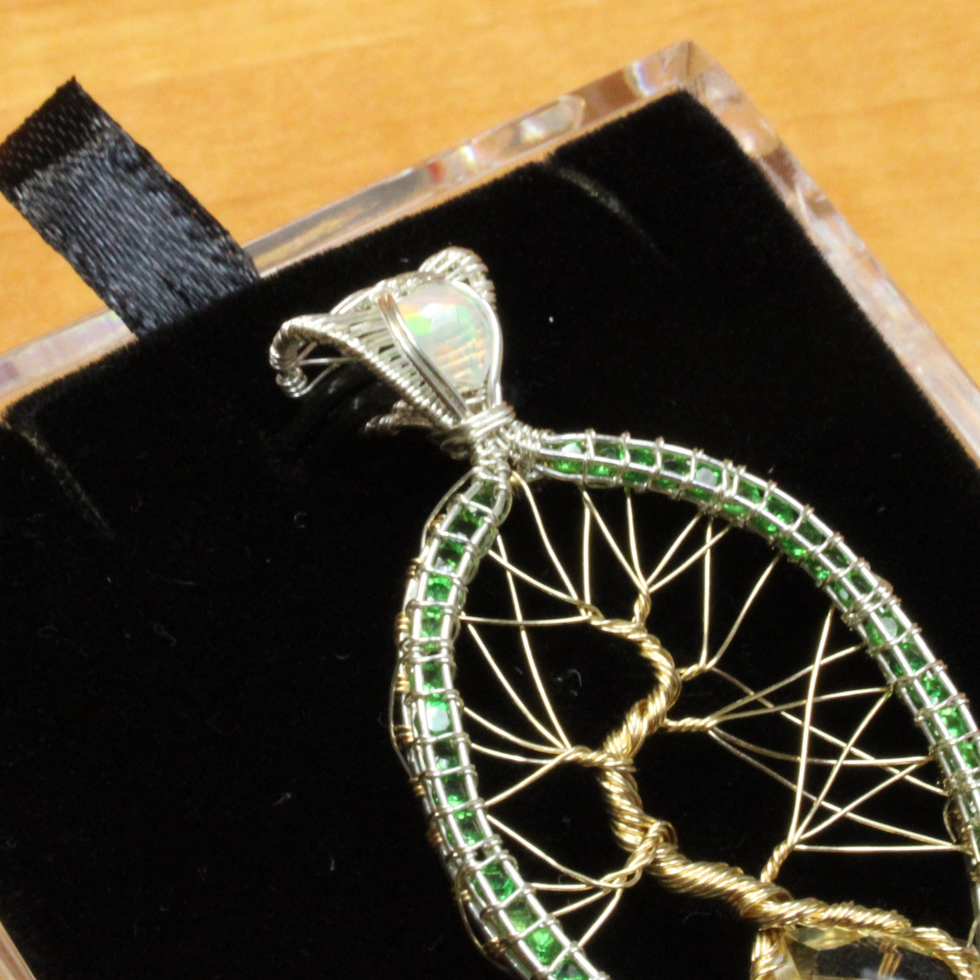 Tsavorite tree of life pendant intricately crafted with green stones and silver wire, elegantly displayed on a black velvet background