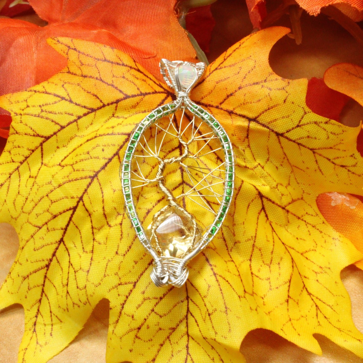 Silver Tsavorite tree of life pendant showcased on a colorful autumn leaf background