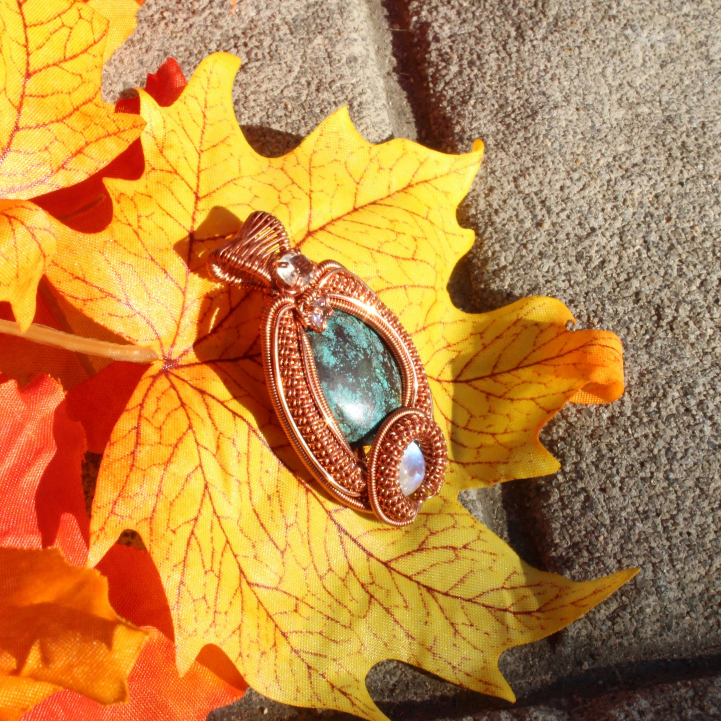 Turquoise copper pendant set on an autumn leaf, showcasing intricate design and vibrant colors