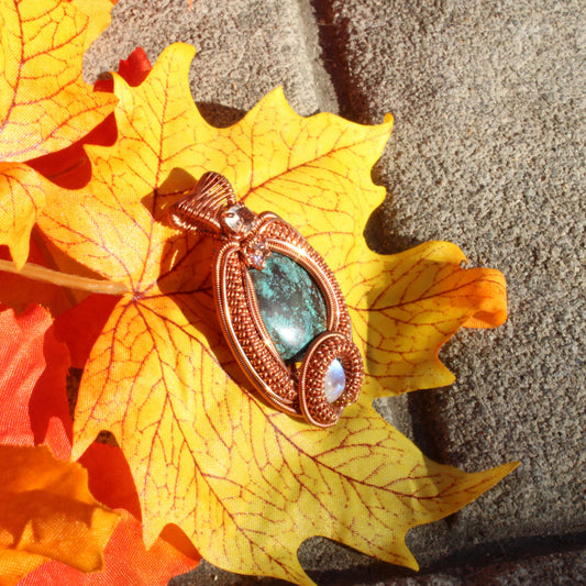 Turquoise copper pendant set on an autumn leaf, showcasing intricate design and vibrant colors