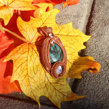 Turquoise copper pendant with intricate design resting on a colorful autumn leaf