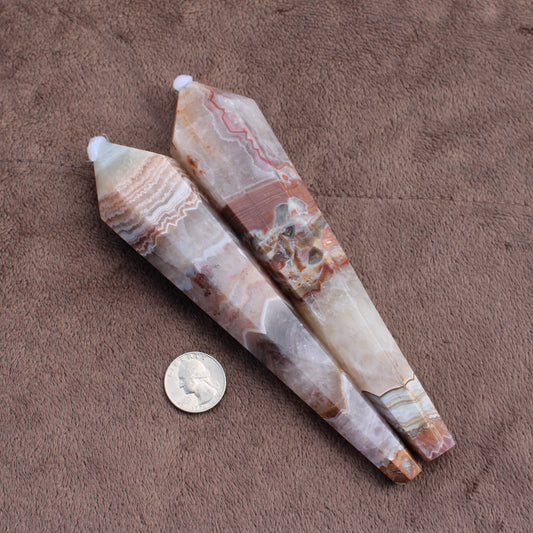 Two polished Crazy Lace Agate Wands with natural patterns displayed next to a quarter for size comparison