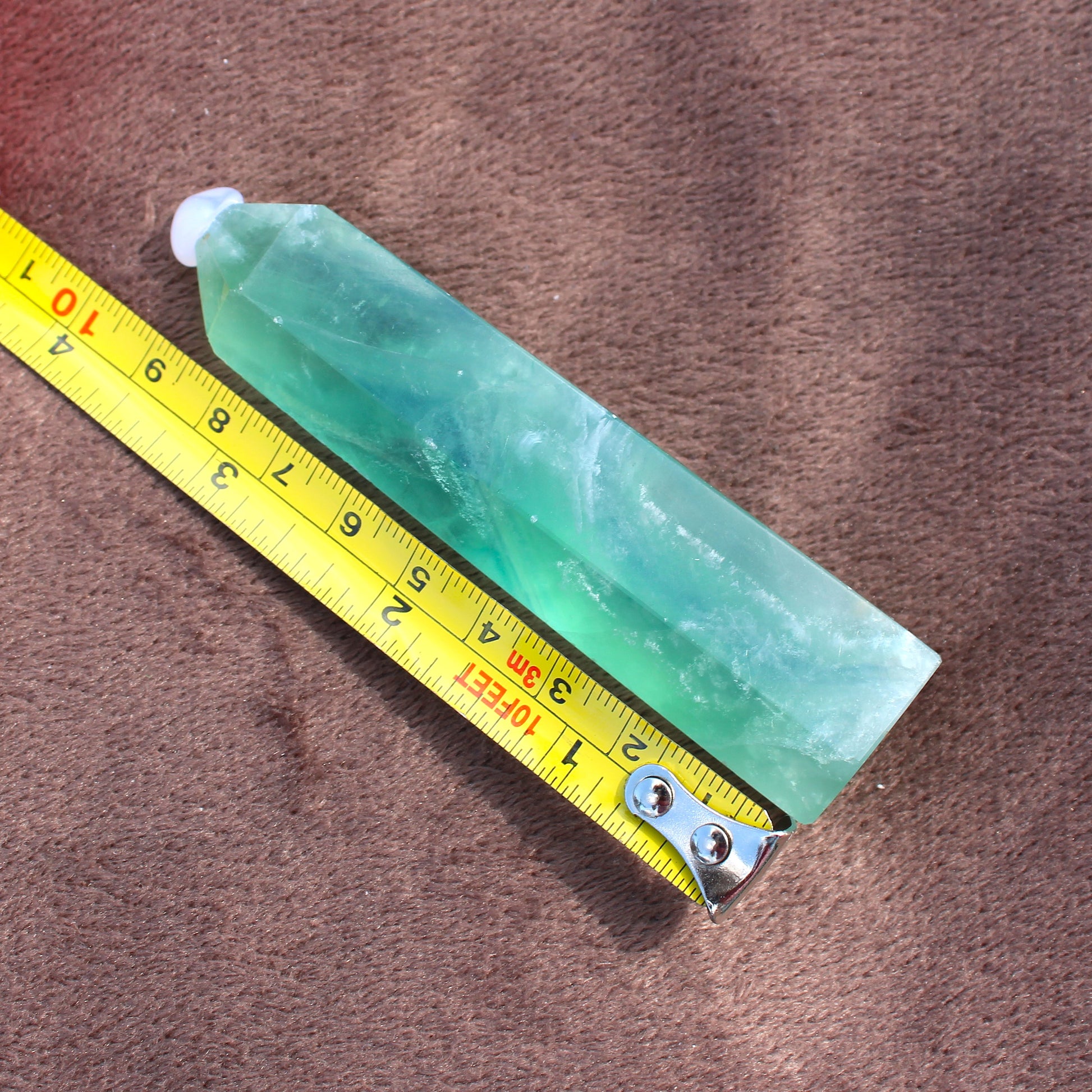 Green Fluorite Tower crystal from Different Branches LLC placed next to a yellow measuring tape on brown fabric