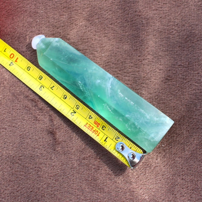 Green Fluorite Tower crystal from Different Branches LLC placed next to a yellow measuring tape on brown fabric