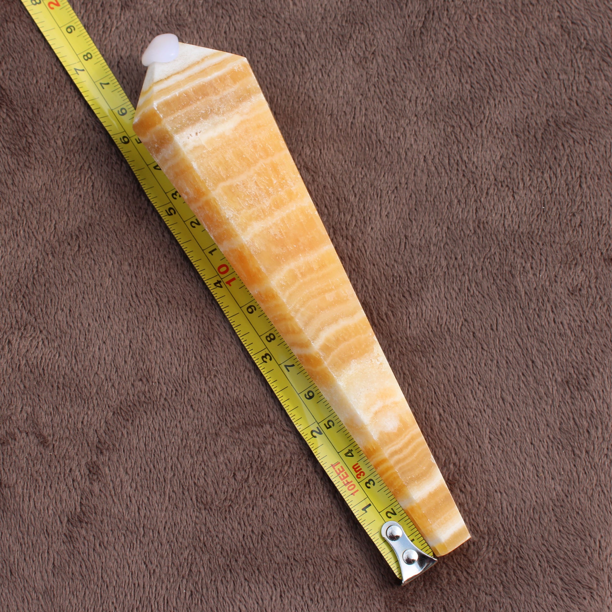 Honey Calcite Wand crystal displayed next to measuring tape on brown fabric background