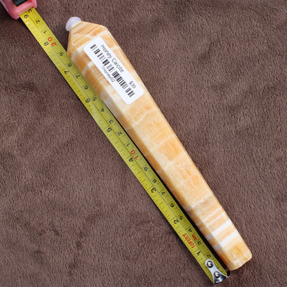 Honey Calcite Wand crystal from Different Branches LLC next to a measuring tape on brown fabric