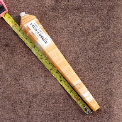 Honey Calcite Wand crystal from Different Branches LLC next to a measuring tape on a brown surface
