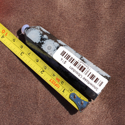 Snowflake Obsidian Tower crystal from Different Branches LLC placed next to a measuring tape on a brown surface