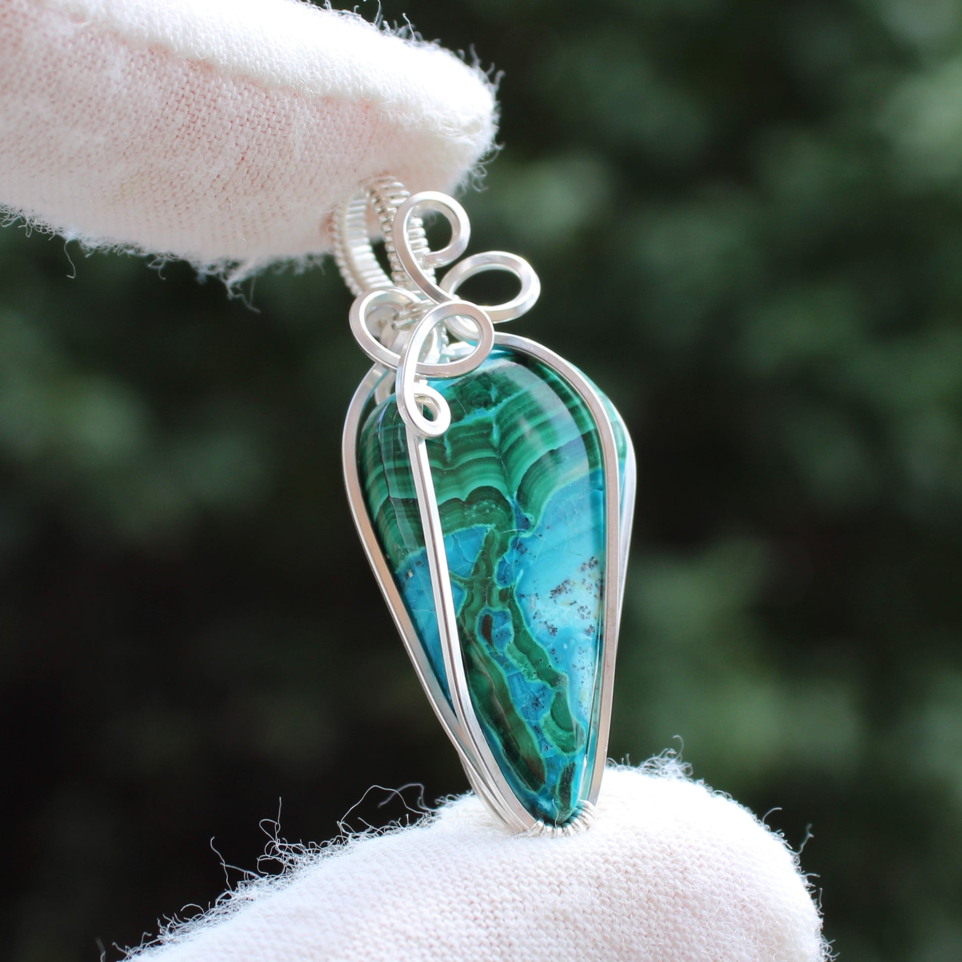 Sterling Silver Chrysocolla Malachite pendant with intricate wire wrapping held by gloved hand