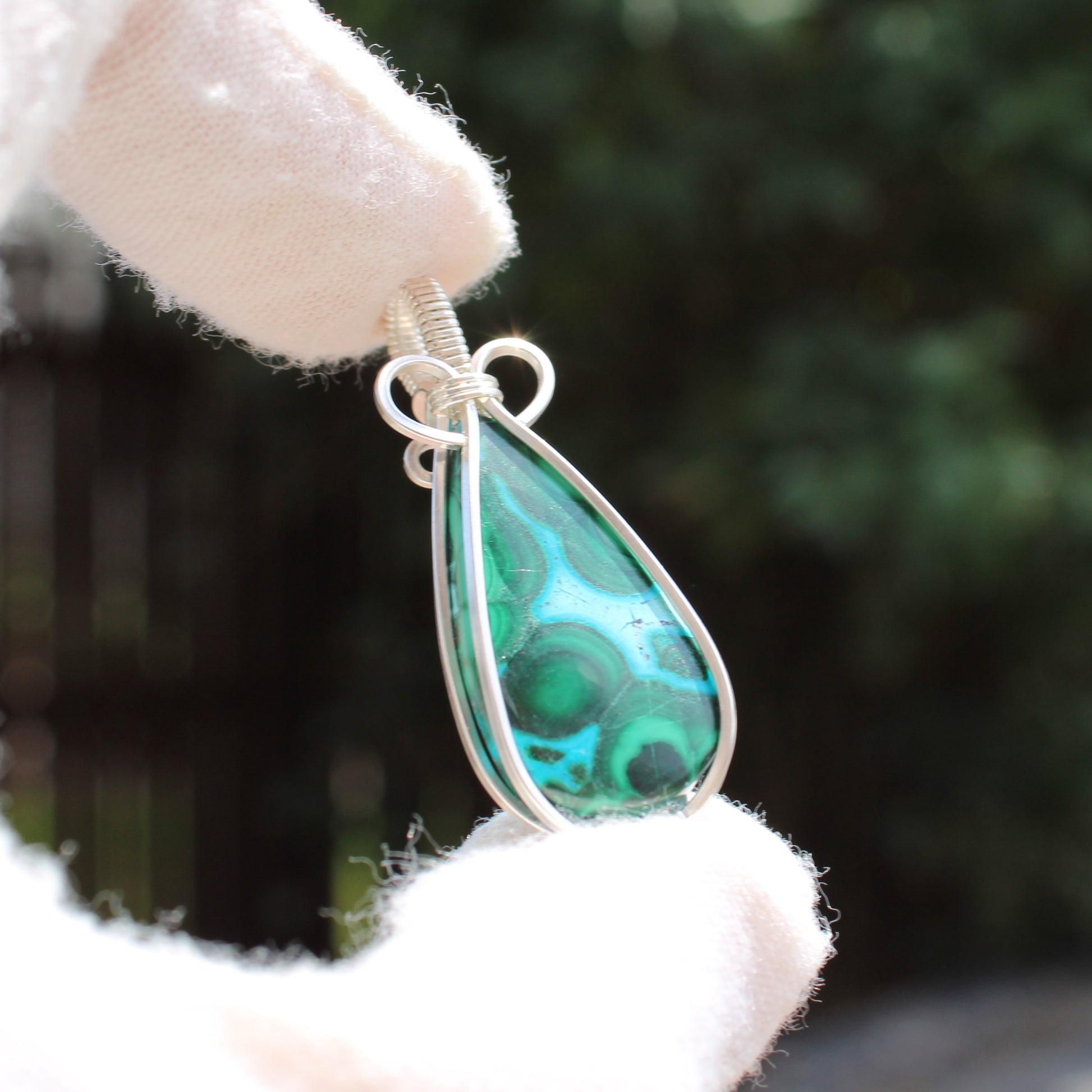 Sterling Silver Chrysocolla Malachite teardrop pendant held by a gloved hand with blurred background