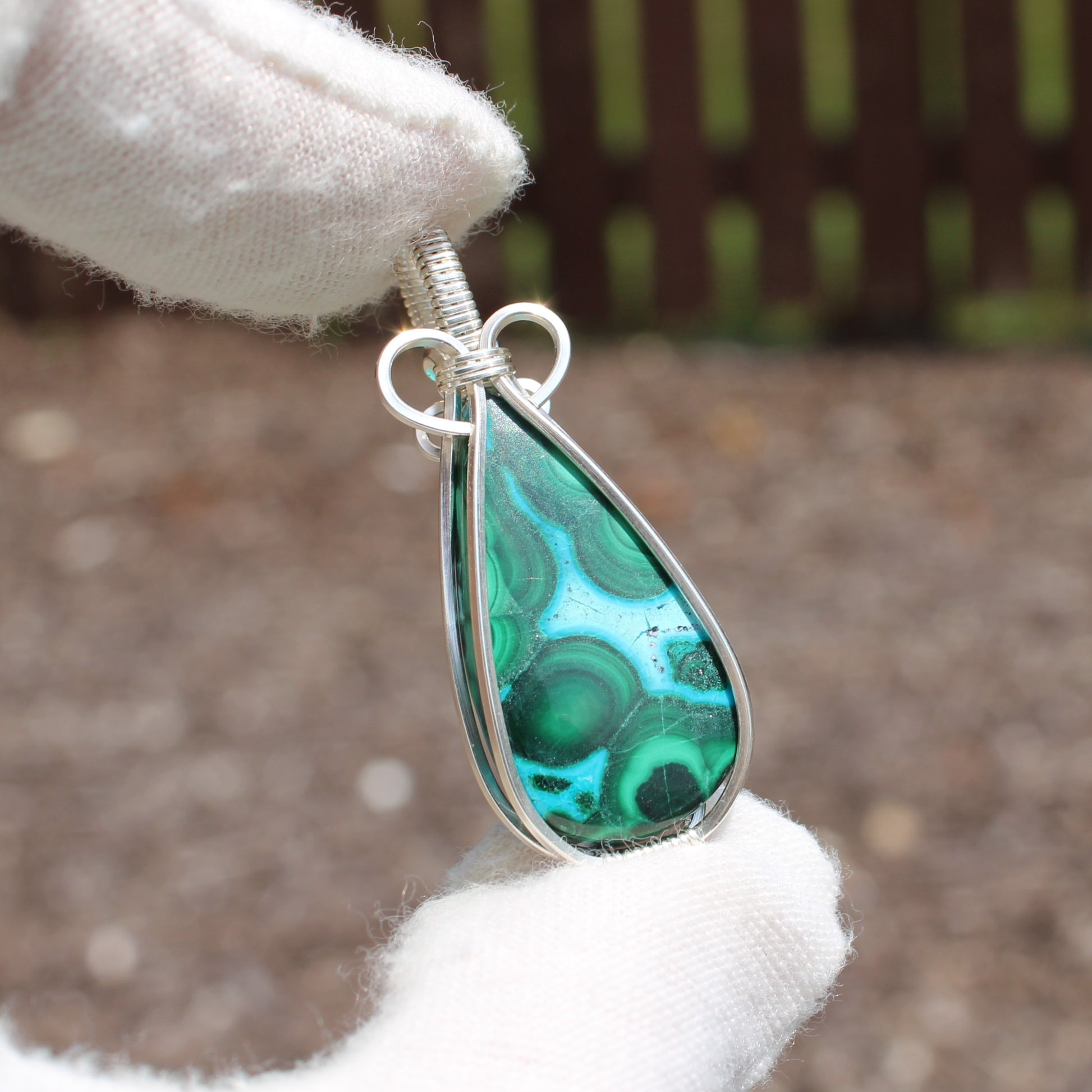 Sterling Silver Chrysocolla Malachite teardrop pendant held by gloved hands with intricate wire wrapping