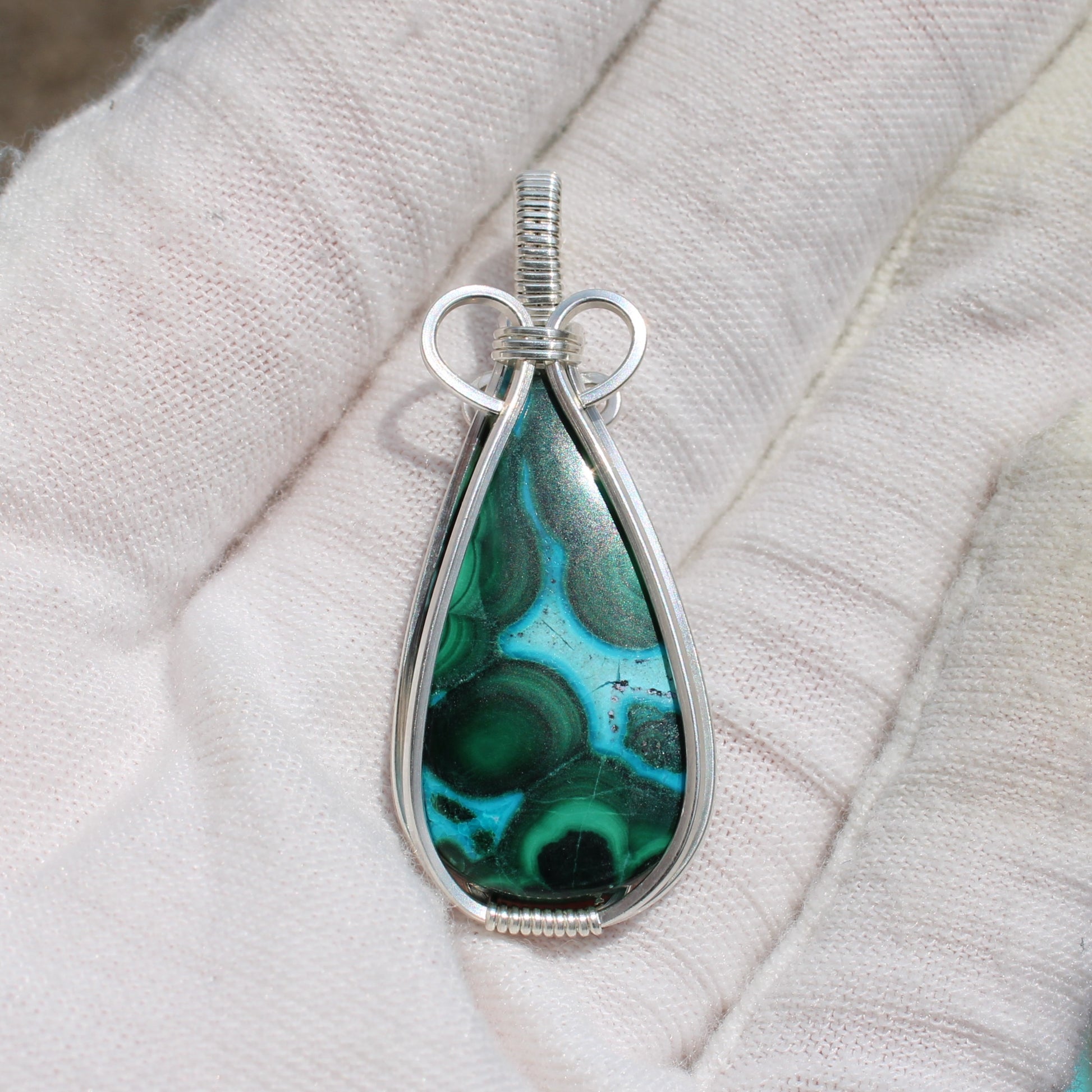 Sterling silver chrysocolla malachite teardrop pendant held in a white-gloved hand