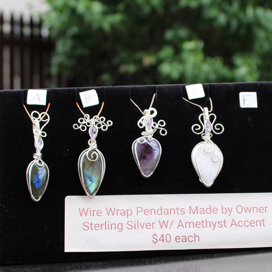 Wire wrap pendants made by owner featuring sterling silver with amethyst accent, displayed on a black stand