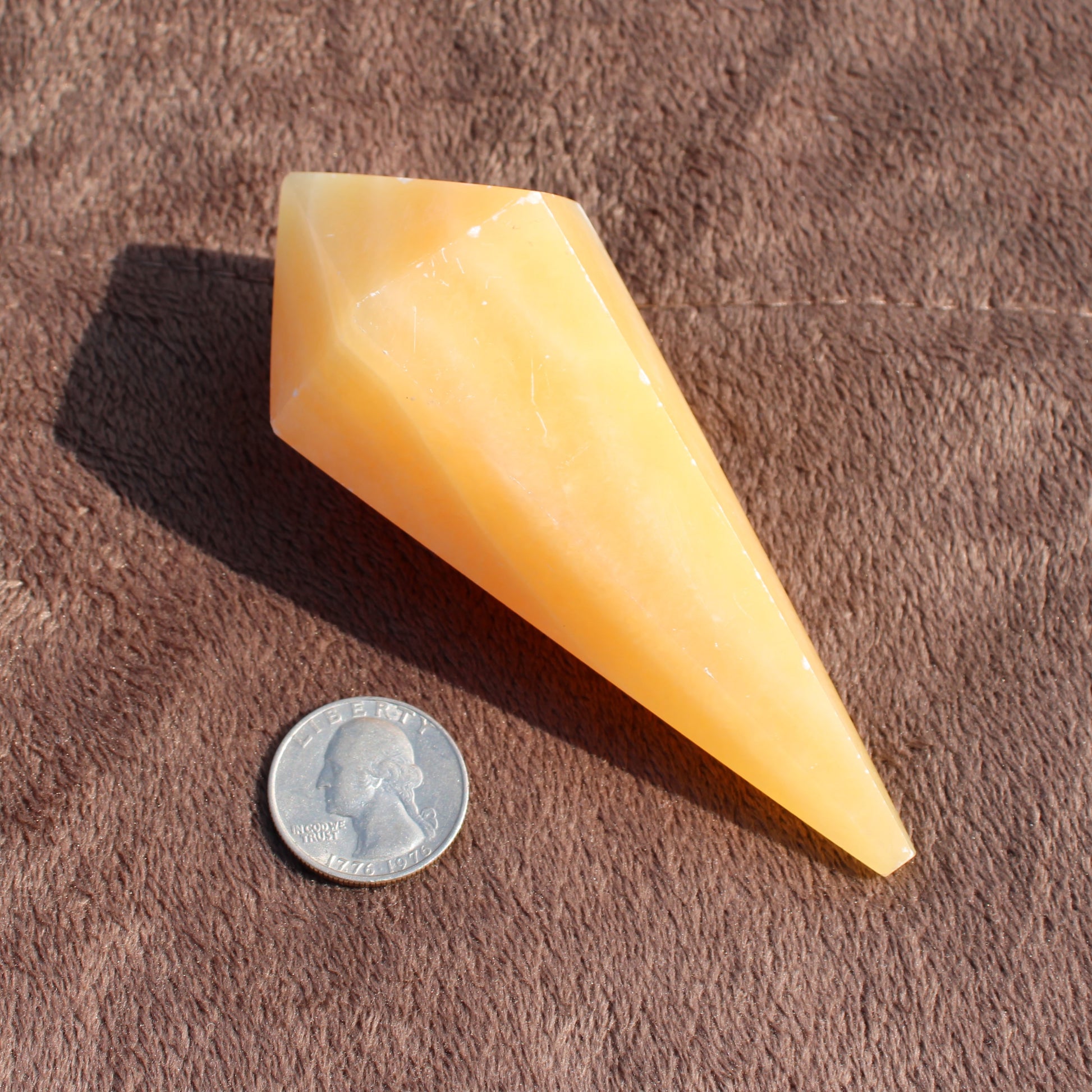 Yellow Calcite Wand crystal next to US quarter for size comparison on brown surface
