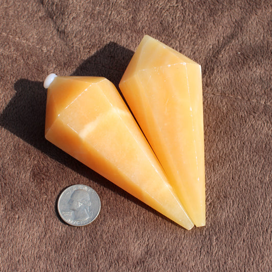 Two yellow calcite wand crystals next to a quarter for size reference on a brown fabric